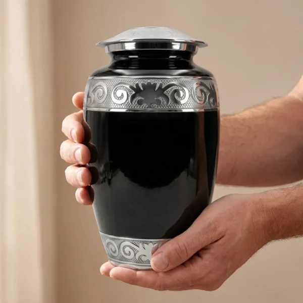 Two hands gently cradling the black enamel adult cremation urn, showing its size