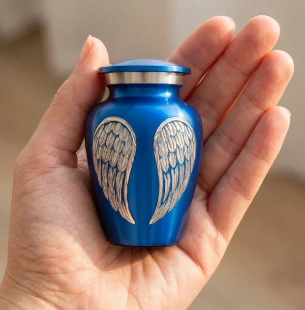 Small blue angel wings keepsake urn resting in an open palm to show its size