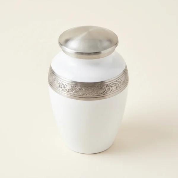 White enamel keepsake urn with an ornate silver engraved band, three-quarter angle